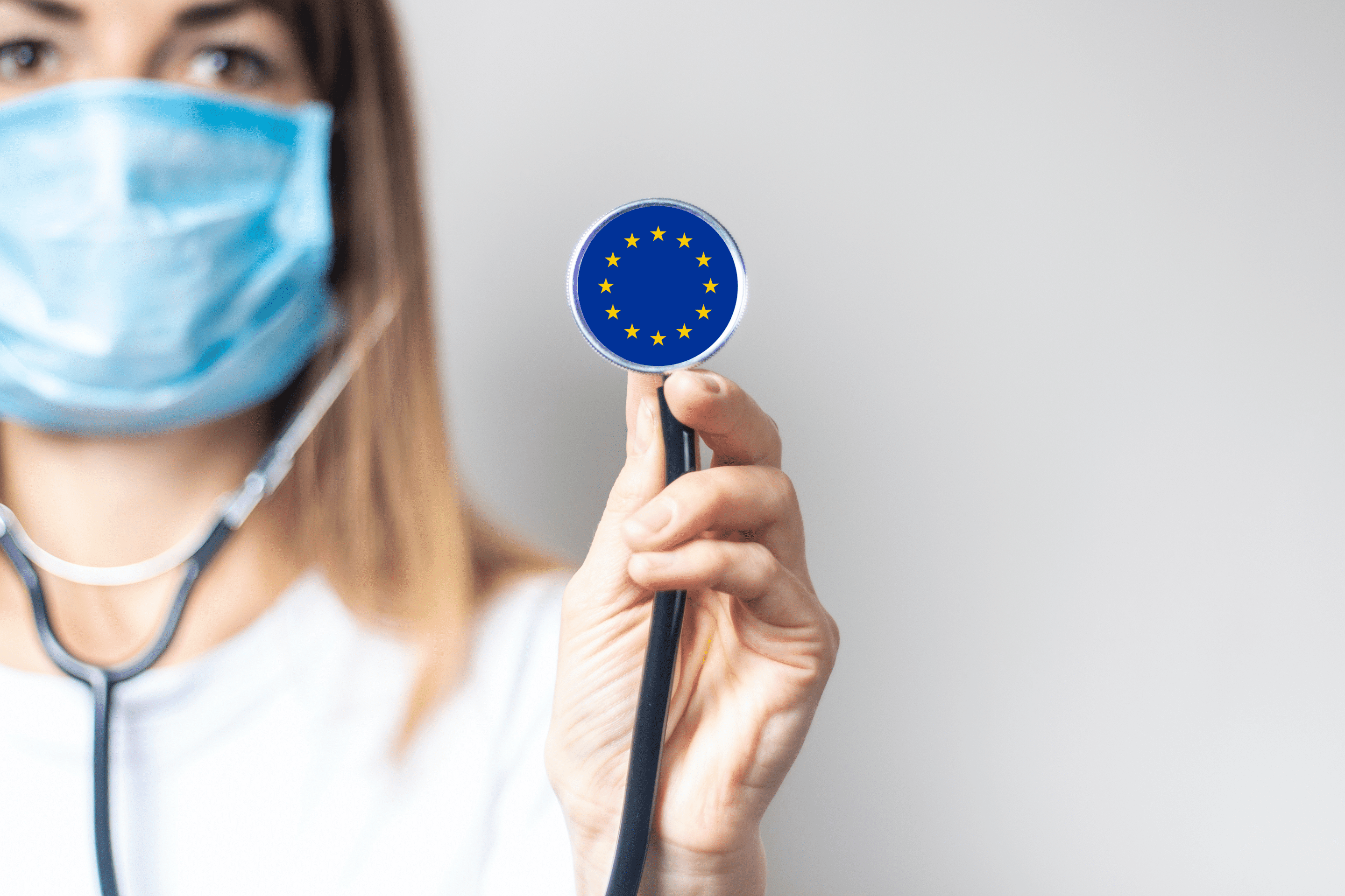 female doctor in a medical mask holds a stethoscope on a light background. Added flag of Europe. Concept medicine, level of medicine, virus, epidemic.