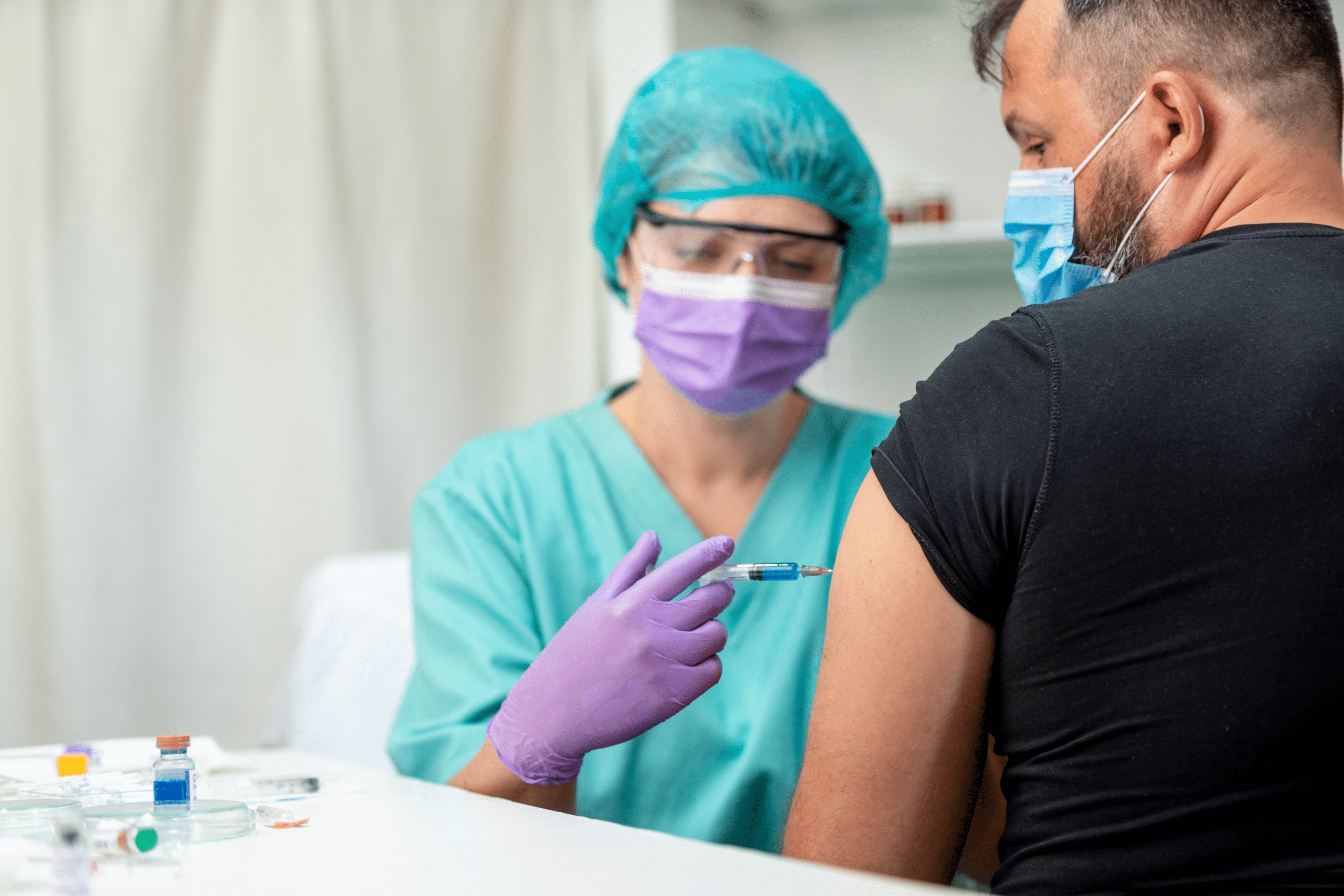 Mid adult man getting flu shot, nurse in protective workwear holding syringe and injecting vaccine in man's arm; prevention and immunization from corona virus infection